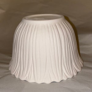 May include: A white ceramic bowl with a tulip-like shape. The bowl has a textured, ridged exterior, and a scalloped base. The bowl is upside down, revealing the smooth interior and the base.