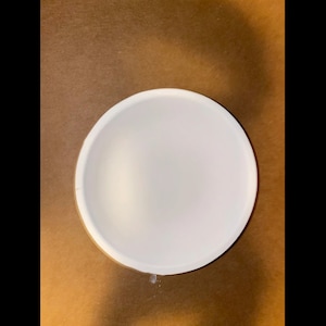 May include: A white, round bowl with a smooth interior. The bowl is set against a brown background. The bowl's shape is a perfect half-sphere, ideal for serving soups, salads, or other dishes.