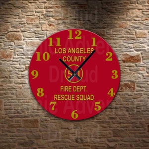 May include: A red wall clock with yellow numerals and hands. The clock face features the text "LOS ANGELES COUNTY FIRE DEPT. RESCUE SQUAD" and a logo. The clock is mounted on a brick wall.