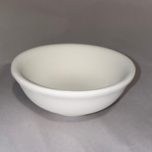 May include: A small, off-white ceramic bowl with a rounded shape and a slightly flared rim. The bowl has a smooth, matte finish and appears to be empty. The bowl is likely used for serving food or as a decorative item.