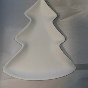 May include: A white ceramic plate in the shape of a Christmas tree. The plate has a smooth surface and a black trim outlining the tree shape. The plate is designed for serving food during the holiday season.