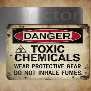 May include: A rectangular metal sign with a distressed, vintage look. The sign features the word "DANGER" in a red and black oval, with the words "TOXIC CHEMICALS" and safety instructions below. A second, plain metal sign is behind it.