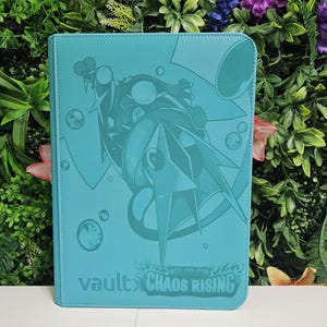 Può includere: Raccoglitore di carte turchese con un'illustrazione dettagliata di una creatura con un design a punte e bolle. Il testo "vault x CHAOS RISING" è stampato in basso. Il raccoglitore è realizzato in materiale strutturato e ha angoli arrotondati.