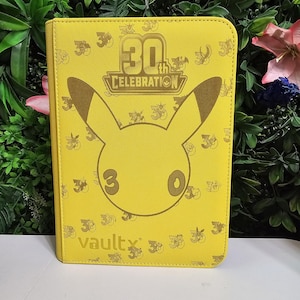 Puede incluir: Una carpeta de tarjetas rectangular de color amarillo brillante que presenta un gran contorno de una cabeza de Pikachu en el centro. Sobre la cabeza está el texto 30th CELEBRATION, y debajo la palabra vaultx. La cubierta tiene un patrón de logos 30th.