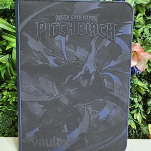 May include: A black rectangular trading card binder featuring the text Mega Evolution Pitch Black and a dark creature graphic. The cover has a textured surface with blue accents and the brand name vaultx printed in the bottom left corner.