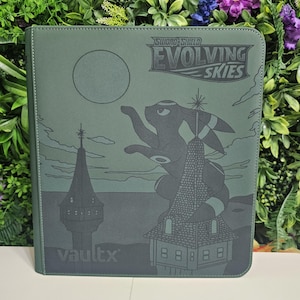 May include: A green card binder with the text "Sword & Shield Evolving Skies" and a graphic of a cartoon character and buildings. The binder has the "vaultx" logo on the bottom left.