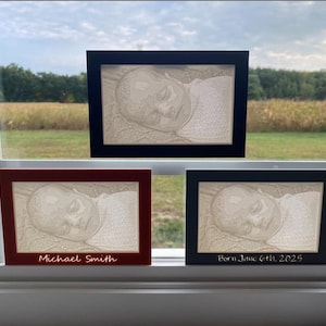 May include: Three framed baby portraits with a 3D effect. One frame is black, one is burgundy, and one is black. The burgundy frame has the name "Michael Smith" on it. The black frame has the text "Born June 6th, 2025".