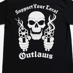 May include: Black t-shirt with a white graphic featuring a skull, two revolvers, and the text "Support Your Local Outlaws". The design has a vintage, biker-inspired aesthetic.