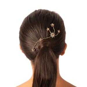 May include: A gold hair comb with a constellation design featuring small stars and a larger star with rhinestones. The comb is in a woman's brown hair, which is pulled back in a ponytail.
