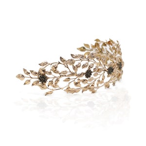 May include: A gold leaf crown headband with black flower accents. The headband is made of metal and has a delicate, feminine design.