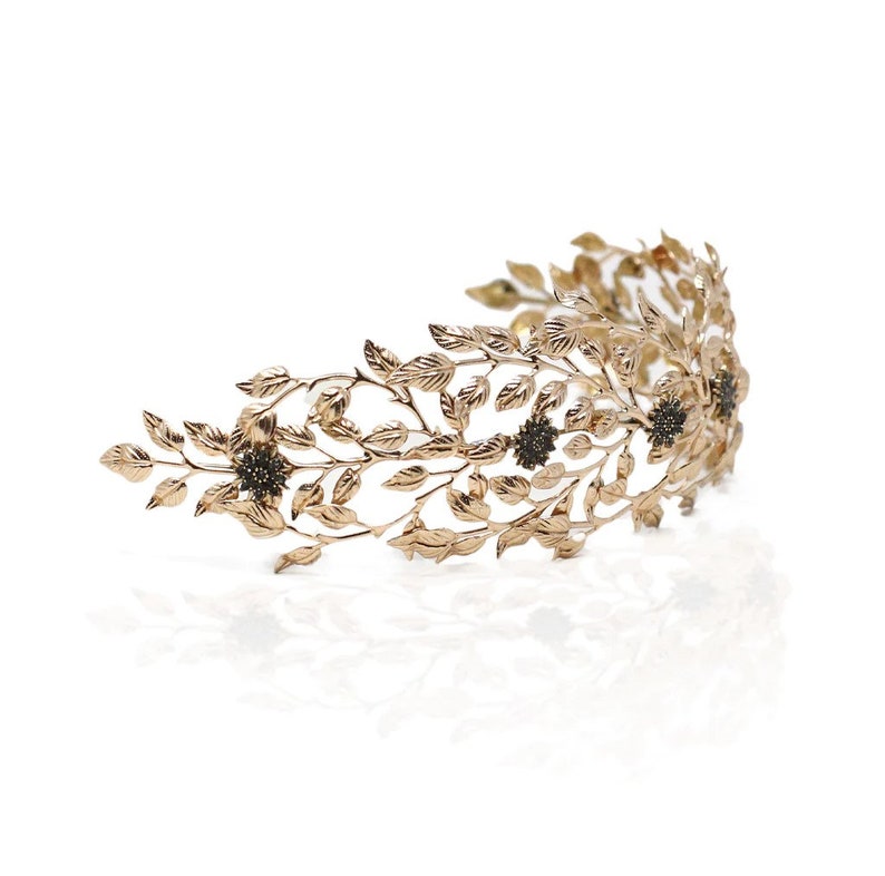 May include: A gold leaf crown headband with black flower accents. The headband is made of metal and has a delicate, feminine design.