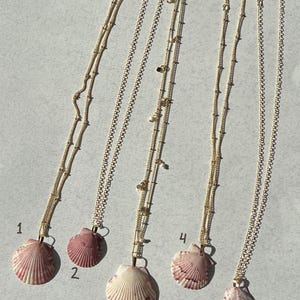 May include: Five gold-toned necklaces, each featuring a unique seashell pendant. The shells vary in shades of pink, white, and brown. The chains are delicate and gold-toned, with some featuring small bead accents. Each necklace is numbered one through five.