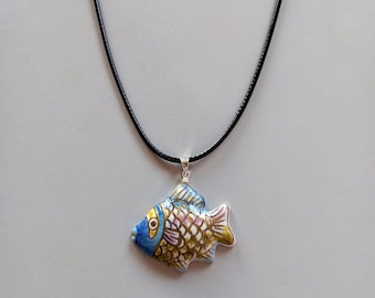 Può includere: Collana con pendente a forma di pesce colorato. Il pendente è un pesce in ceramica con squame blu, gialle, rosa e bianche. Il pesce è appeso a una collana con cordino nero.
