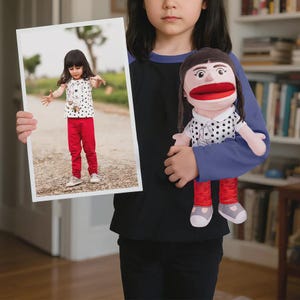 May include: A child holding a framed photograph and a puppet. The photograph shows a young girl in a white shirt with black polka dots, red pants, and silver shoes. The puppet has a large red mouth, brown hair, and a similar outfit.