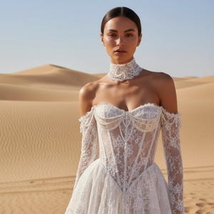May include: A white lace wedding dress with off-the-shoulder sleeves and a corset bodice. The dress features intricate floral lace detailing and a full skirt. A matching lace choker is worn around the neck. The background is a desert landscape.