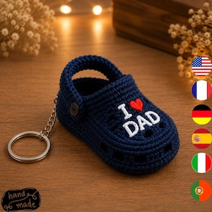 May include: A dark blue crocheted clog keychain featuring a small red heart and the white embroidered text I DAD. The miniature shoe has a classic perforated design, a pivoting heel strap with a dark button, and a silver metal keyring attached.