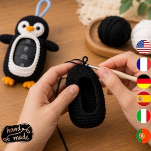 May include: A black and white crocheted penguin-shaped car key fob cover with a light blue loop at the top and orange feet. A second black crocheted piece is being worked on with a silver crochet hook and black yarn.