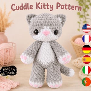 May include: A gray and white crocheted cat plush toy with large black eyes and a pink nose. The cat has white patches on its face, chest, and paws, with small pink paw pads. The text Cuddle Kitty Pattern is displayed at the top of the image.