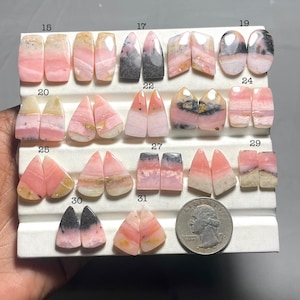 May include: A selection of pink and white gemstone pairs, each with unique patterns and shapes, presented on a white surface. Some stones have grey or black accents. A coin is included for size reference. The gemstones are numbered 15 to 31.