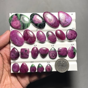 Peut inclure: Une collection de pierres précieuses polies en rubis et zoïsite de différentes formes, dont ovales, en goutte et carrées. Les pierres présentent un mélange de teintes rouge foncé et verte, avec une pièce de monnaie pour la comparaison de taille.