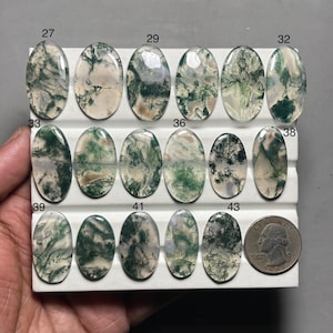 May include: A collection of oval-shaped moss agate gemstones in various shades of green and white, displayed on a white surface. Each stone has unique patterns. A US quarter is included for size reference.