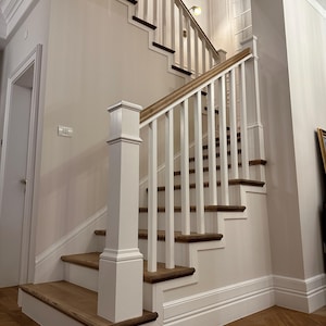 Könnte beinhalten: Eine Holztreppe mit weißen Balustern und einem hellbraunen Handlauf. Die Stufen sind aus hellbraunem Holz mit dunkelbraunen Zierleisten gefertigt. Die Wände sind hellbeige gestrichen. Der Boden hat ein Fischgrätmuster.