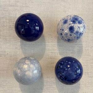 Op de afbeelding: Vier bolvormige keramische objecten in een rasteropstelling. Linksboven een effen glanzend donkerblauwe bol. Rechtsboven een witte bol met blauwe kristallijne vlekken. Linksonder een lichtblauw bellenpatroon. Rechtsonder een diepblauwe bol met witte vlekken.