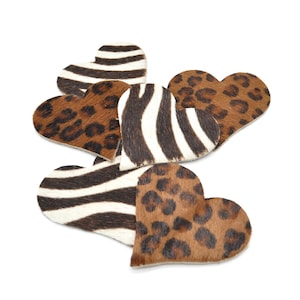 Può includere: Una collezione di decorazioni a forma di cuore. Alcune presentano un motivo a strisce zebrate in bianco e nero, mentre altre mostrano una stampa leopardata marrone e nera. I pezzi sono disposti su uno sfondo bianco.