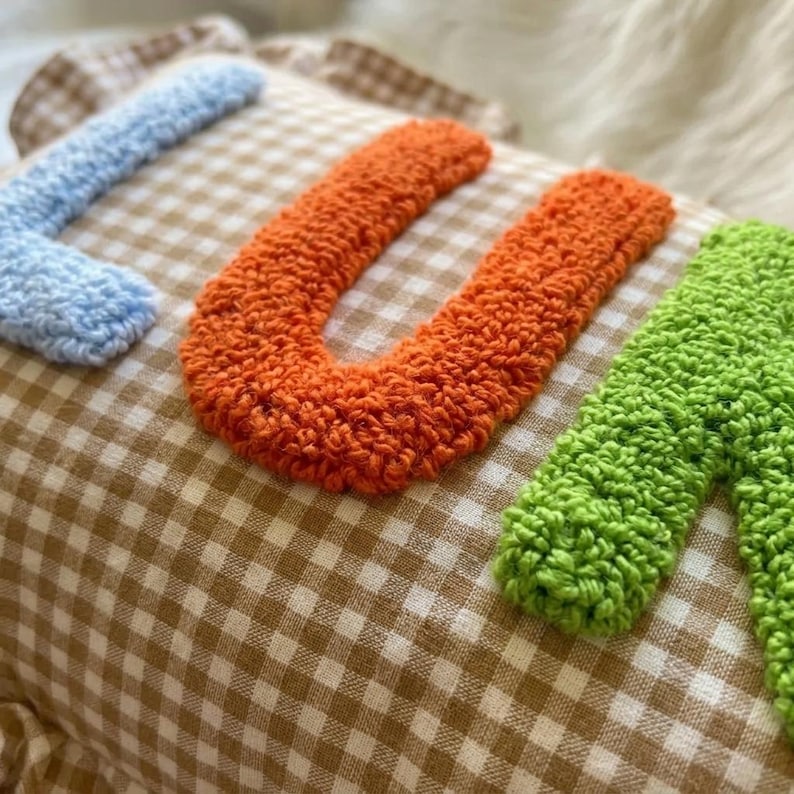 May include: A decorative pillow with the word "LUV" embroidered in blue, orange, and green yarn. The pillow has a brown and white checkered pattern.