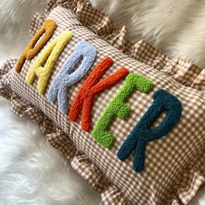 May include: A decorative pillow with the name "PARKER" embroidered in colorful, textured letters. The pillow has a brown and white checkered pattern and a ruffled edge.