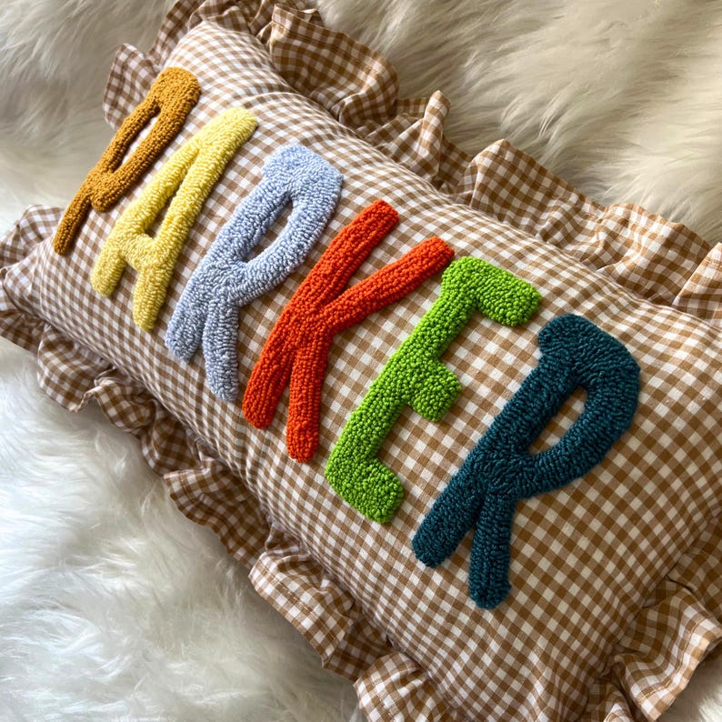 May include: A decorative pillow with the name "PARKER" embroidered in colorful, textured letters. The pillow has a brown and white checkered pattern and a ruffled edge.