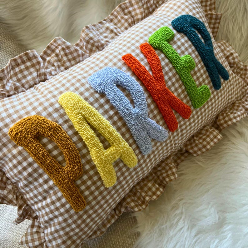 May include: A rectangular decorative pillow with the word "PARTY" embroidered in colorful, textured letters. The pillow has a brown and white gingham pattern and a ruffled edge.