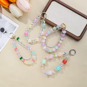 May include: Four beaded wristlet keychains in pastel colors. Each keychain features a variety of colorful beads, including iridescent, round, and faceted beads. The keychains have gold or silver-colored metal rings for attaching keys.