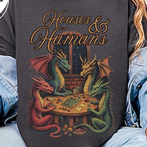 May include: Graphite-colored sweatshirt featuring a fantasy illustration of four dragons playing a tabletop game. The text "Houses & Humans" is above the scene. The dragons are red, green, blue, and gold. The sweatshirt has "Comfort Colors" branding.