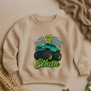May include: Beige crewneck sweatshirt featuring a green monster truck graphic with the number 3, checkered flags, and the name "Ethan" in green script. The truck has large black tires with orange accents.