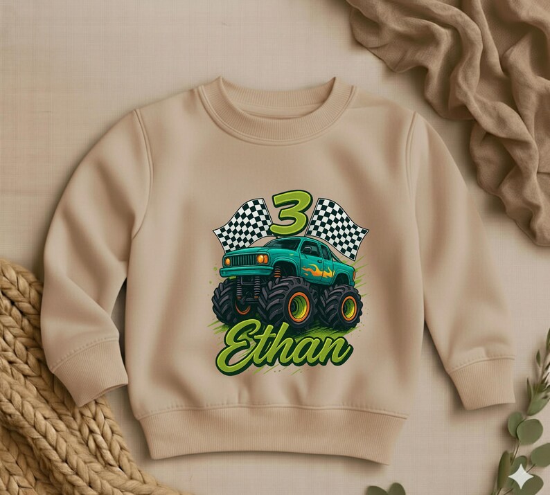 May include: Beige crewneck sweatshirt featuring a green monster truck graphic with the number 3, checkered flags, and the name "Ethan" in green script. The truck has large black tires with orange accents.