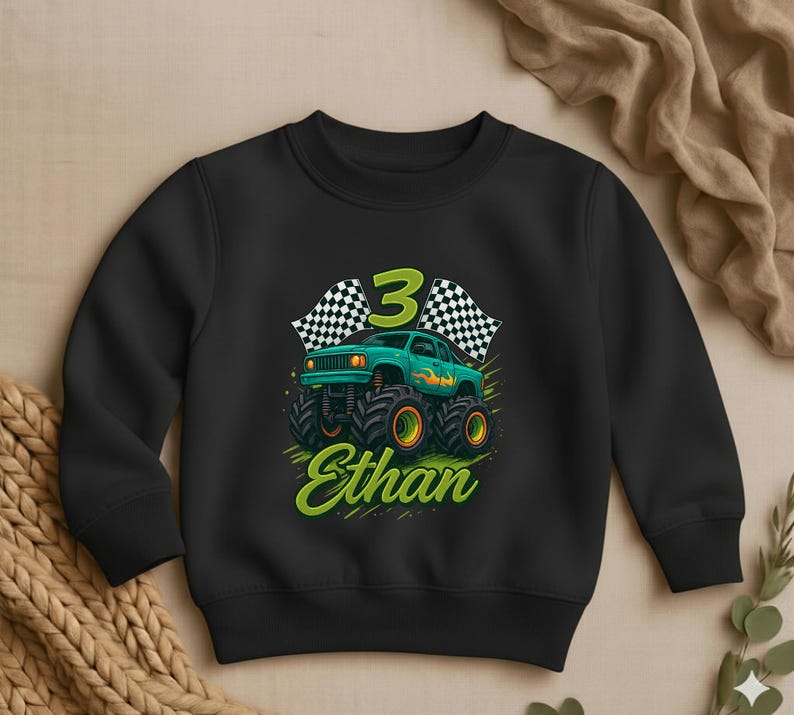 May include: Black sweatshirt with a graphic of a green monster truck with orange wheels, the number 3, and checkered flags. The name "Ethan" is written in green script below the truck.