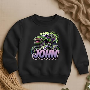 May include: Black sweatshirt featuring a monster truck design with the name "JOHN" in a purple and white font. The monster truck is green and purple with flames and a menacing grin.
