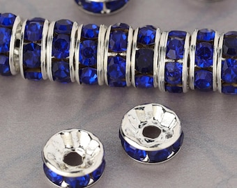 May include: A close-up of a silver and blue rhinestone bead. The bead is round and has a hole in the center. The bead is surrounded by other similar beads.