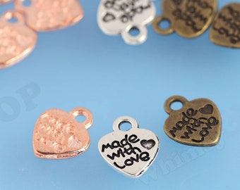 May include: Assortment of heart-shaped metal charms with the words "Made with Love" engraved on them. The charms are in silver, gold, and rose gold tones.