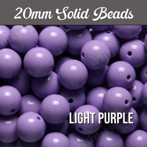 May include: A close-up of a pile of 20mm solid light purple beads. The beads are round and have a smooth, glossy finish.
