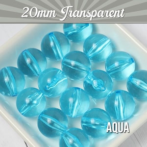 May include: A close-up of 20mm transparent aqua blue round beads. The beads are made of acrylic and have a smooth, shiny finish. The beads are arranged in a circle on a white surface.