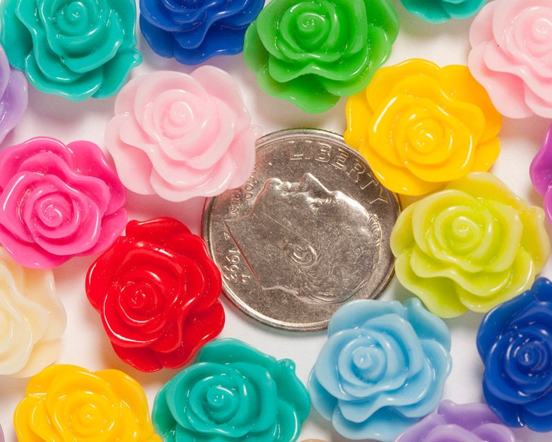 May include: Assortment of colorful plastic rose-shaped embellishments. The roses are in various colors, including pink, red, yellow, green, blue, and purple. The roses are approximately the size of a US dime.