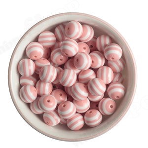 K&ouml;nnte beinhalten: Eine Sch&uuml;ssel gef&uuml;llt mit runden, rosa und wei&szlig; gestreiften Perlen. Die Perlen sind aus Silikon und eignen sich perfekt f&uuml;r die Herstellung von Schmuck oder anderen Bastelarbeiten.