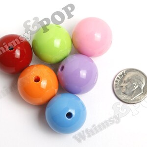 May include: Six colorful plastic beads, each with a hole in the center. The beads are red, green, pink, purple, orange, and blue. A silver US dime is included for size comparison.