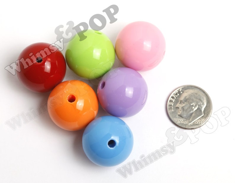 May include: Six colorful plastic beads, each with a hole in the center. The beads are red, green, pink, purple, orange, and blue. A silver US dime is included for size comparison.