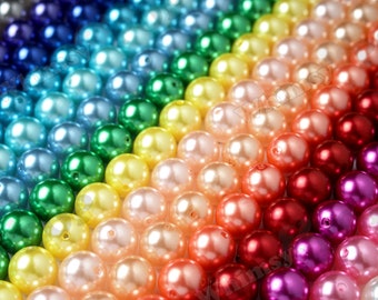 May include: A vibrant display of spherical beads arranged in a rainbow spectrum. The colours range from deep blues and greens to yellows, oranges, and reds. Each bead has a glossy, pearlescent sheen and a small central hole.