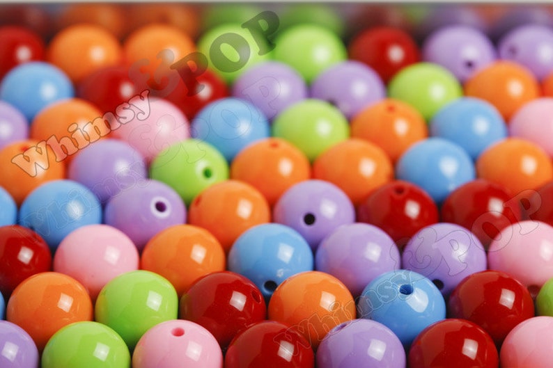 May include: A close-up of a variety of colorful round beads. The beads are made of plastic and have a glossy finish. The colors include red, orange, yellow, green, blue, purple, and pink.