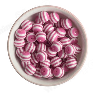 K&ouml;nnte beinhalten: Eine Sch&uuml;ssel gef&uuml;llt mit runden, rosa-wei&szlig; gestreiften Perlen. Die Perlen sind aus Kunststoff und haben eine gl&auml;nzende Oberfl&auml;che.