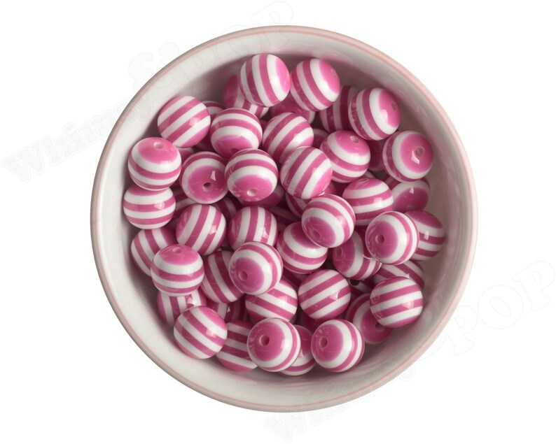 K&ouml;nnte beinhalten: Eine Sch&uuml;ssel gef&uuml;llt mit runden, rosa-wei&szlig; gestreiften Perlen. Die Perlen sind aus Kunststoff und haben eine gl&auml;nzende Oberfl&auml;che.